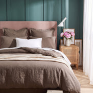 Warm taupe washed linen bedding on a bed with a blush headboard against teal panelling
