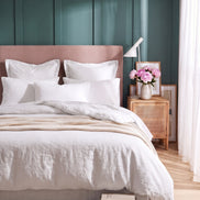 Warm white washed linen bedding on a bed with a blush headboard against teal panelling