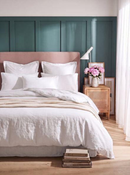 Warm white washed linen bedding on a bed with a blush headboard against teal panelling
