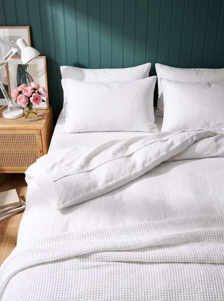 Warm white washed linen bedding, close view against deep green panelling