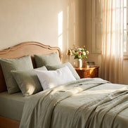 Sage green washed linen bedding in morning light, carved headboard
