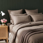 Warm taupe washed linen bedding against deep green panelling, evening
