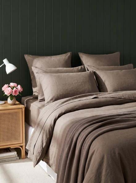 Warm taupe washed linen bedding against deep green panelling, evening