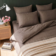 Warm taupe washed linen bedding against deep green panelling, daylight