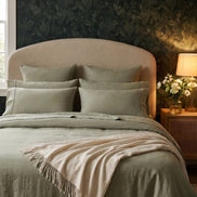 Sage green washed linen bedding against dark floral wallpaper, cream throw