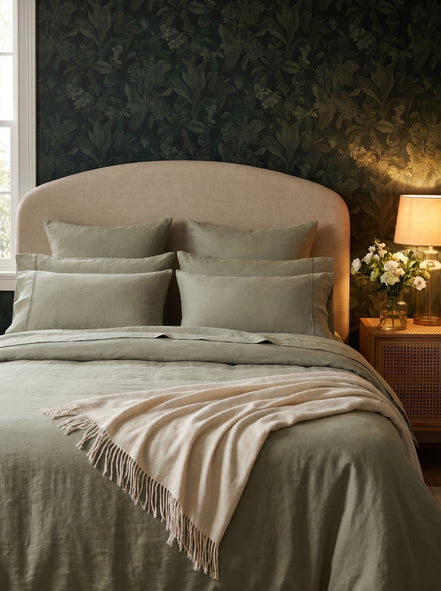 Sage green washed linen bedding against dark floral wallpaper, cream throw