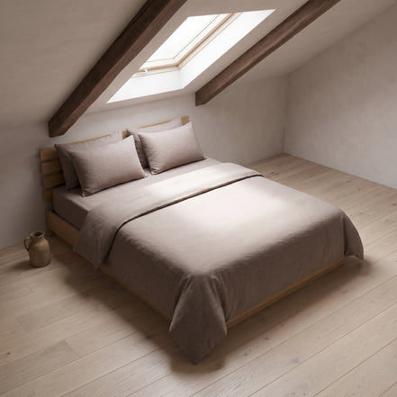 Taupe duvet cover on a low wooden bed in an attic room with a sloping ceiling