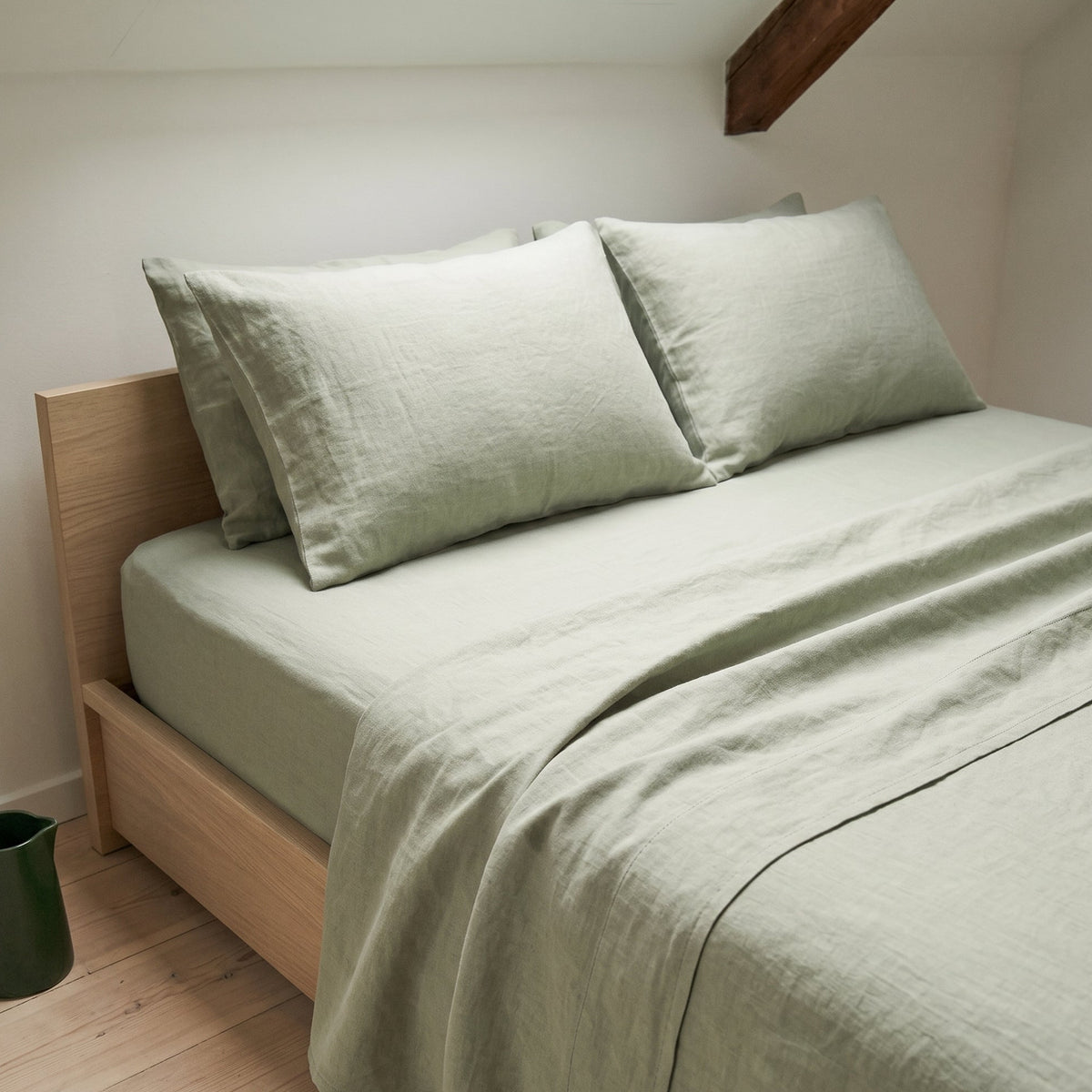 Sage green duvet cover on a low wooden bed in an attic room with a sloping ceiling