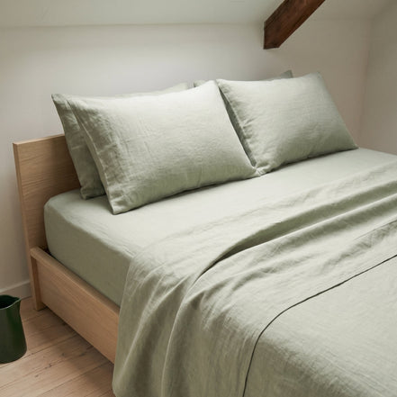 Sage green duvet cover on a low wooden bed in an attic room with a sloping ceiling