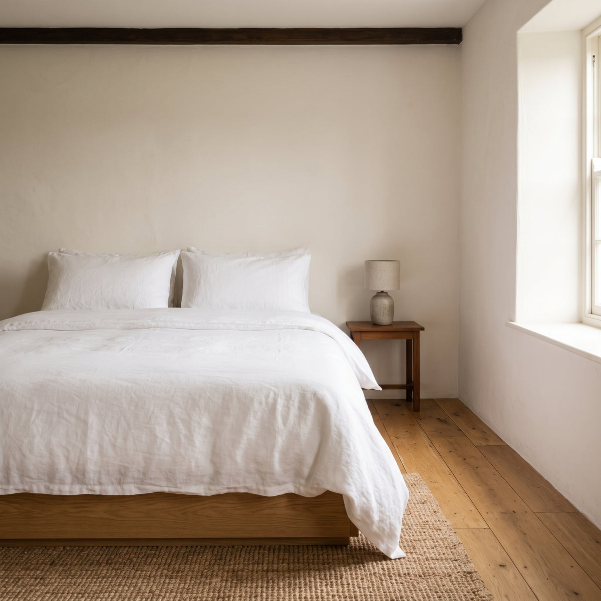 Warm white duvet cover on a low wooden bed beside a curtained window