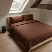 Deep brown duvet cover on a low wooden bed beside a curtained window