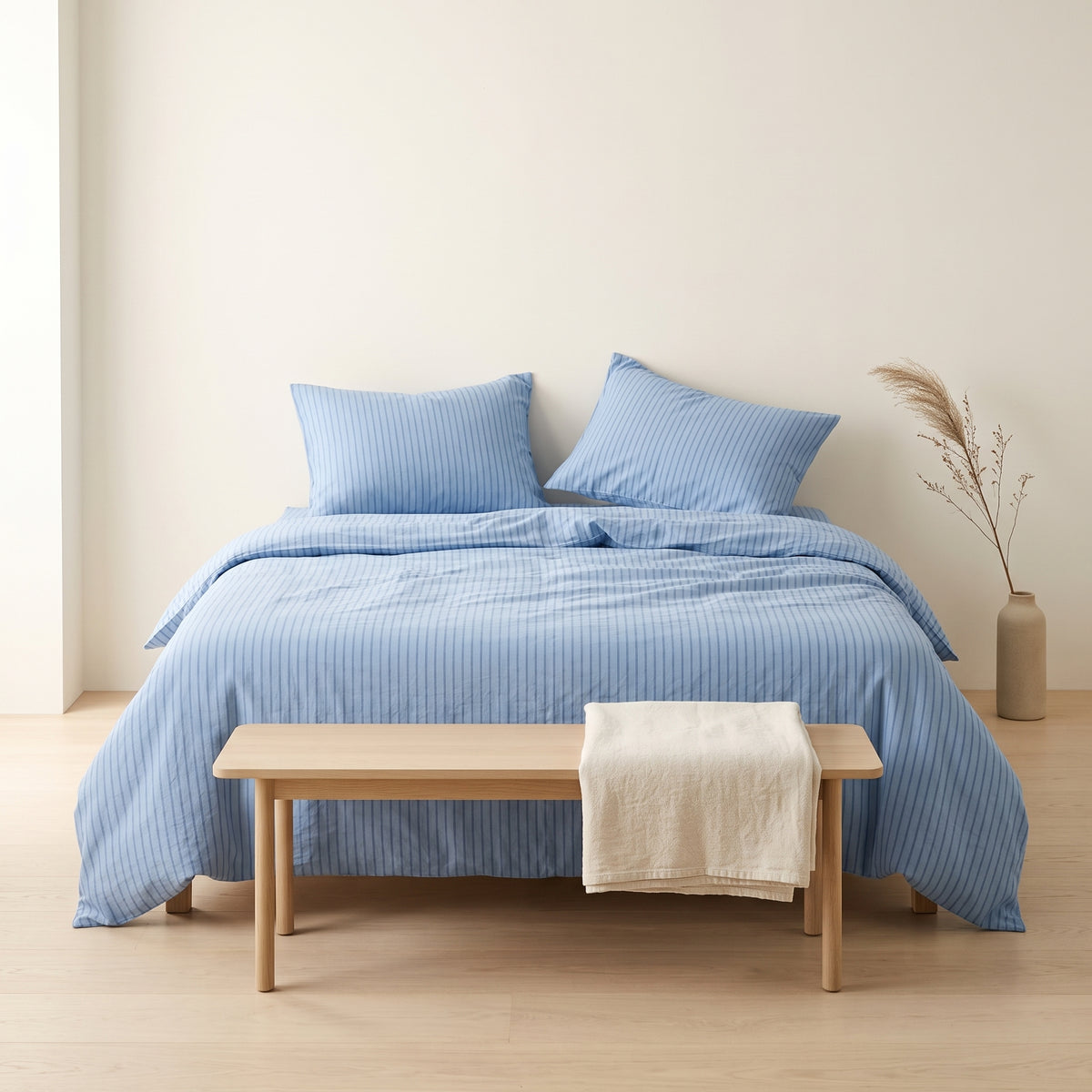 Side view of a bed made up in pale blue striped bedding
