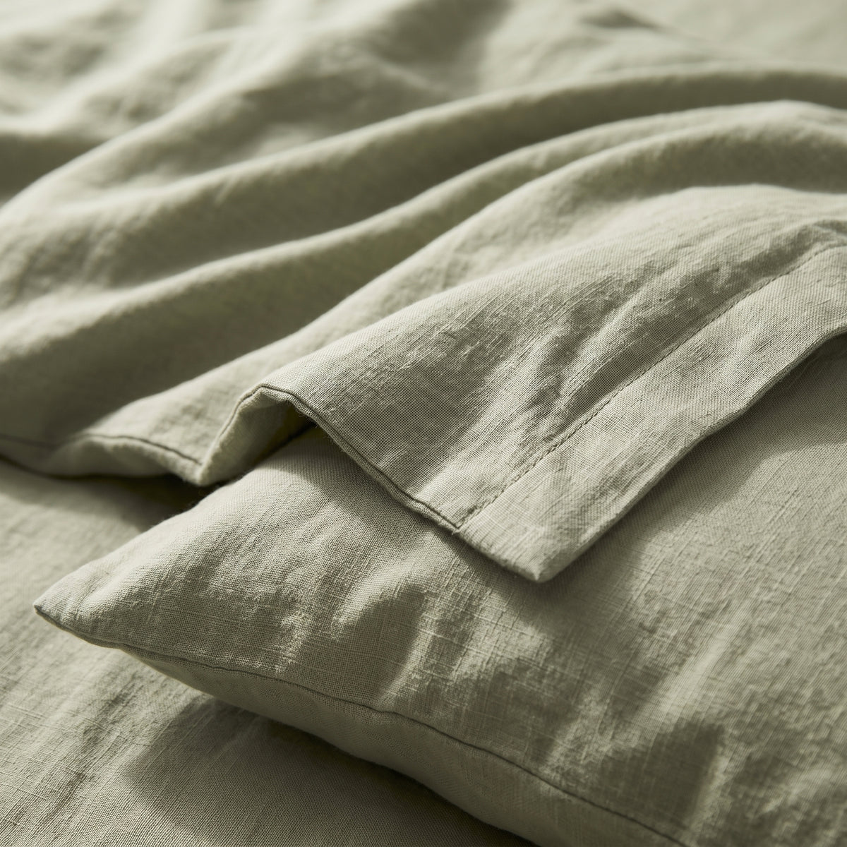 Close view of the sage green linen folded back over a pillow