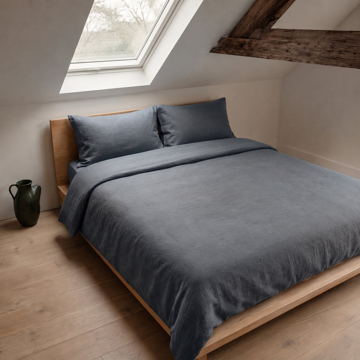 Slate grey duvet cover on a low wooden bed beneath a sloped ceiling and skylight
