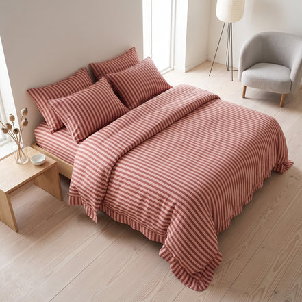 Terracotta striped bedding photographed in a quiet bedroom with pale wood flooring
