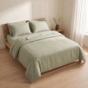 Sage green washed linen bedding on a low oak bed beside a window