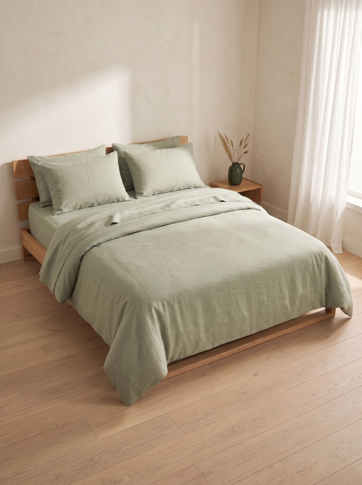 Sage green washed linen bedding on a low oak bed beside a window