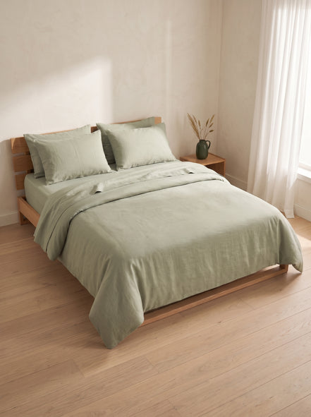 Sage green washed linen bedding on a low oak bed beside a window
