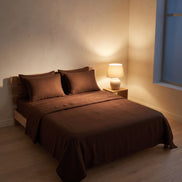 Deep brown washed linen bedding in a bedroom at night, one lamp lit