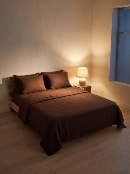Deep brown washed linen bedding in a bedroom at night, one lamp lit